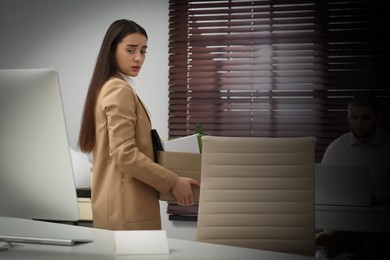 Upset dismissed woman carrying box with personal stuff in office