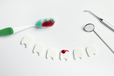 Composition of dental instruments, decorative teeth and toothbrush with blood on white background, top view. Gum inflammation