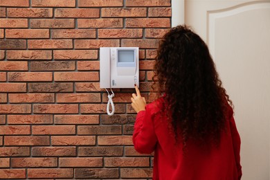 Photo of African-American woman pressing button on intercom panel indoors, back view