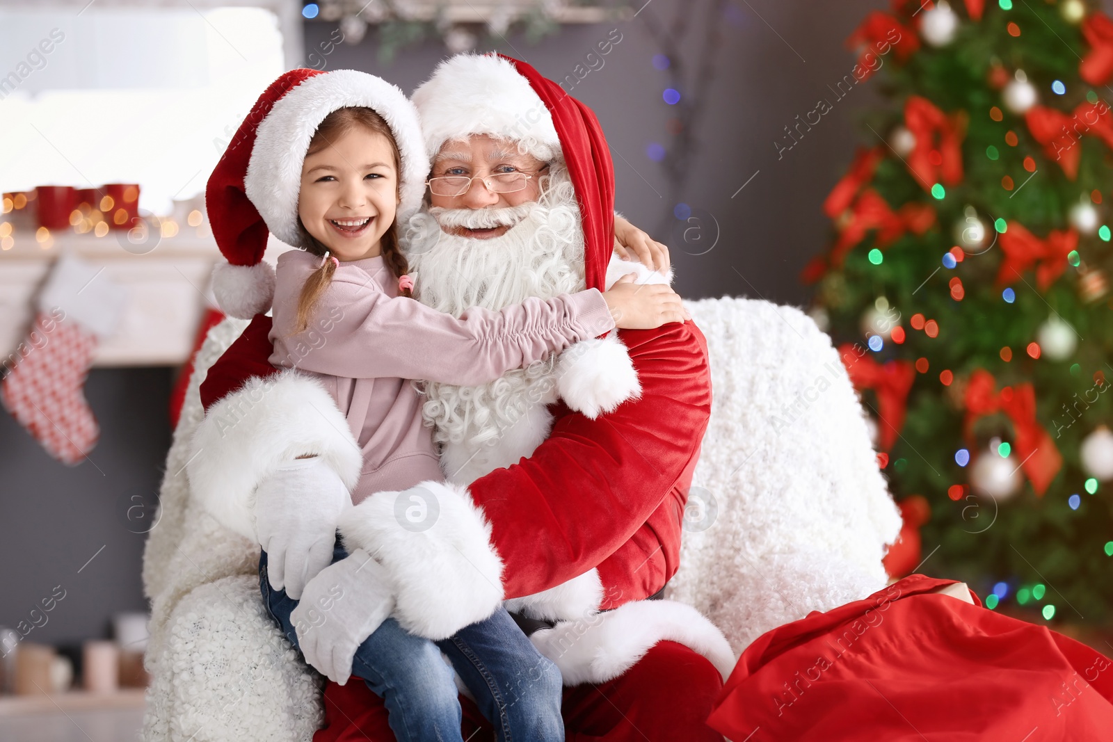 Photo of Little girl sitting on authentic Santa Claus' lap indoors