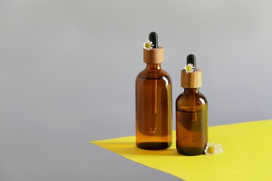 Photo of Bottles of chamomile essential oil and flowers on color background, space for text