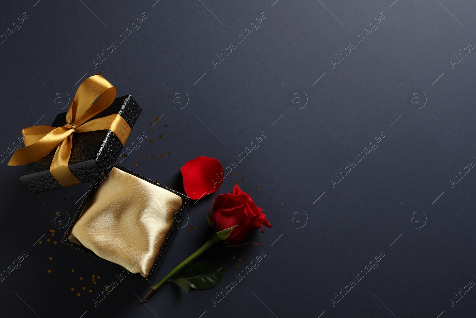 Photo of Open gift box and red rose on black background, flat lay. Space for text