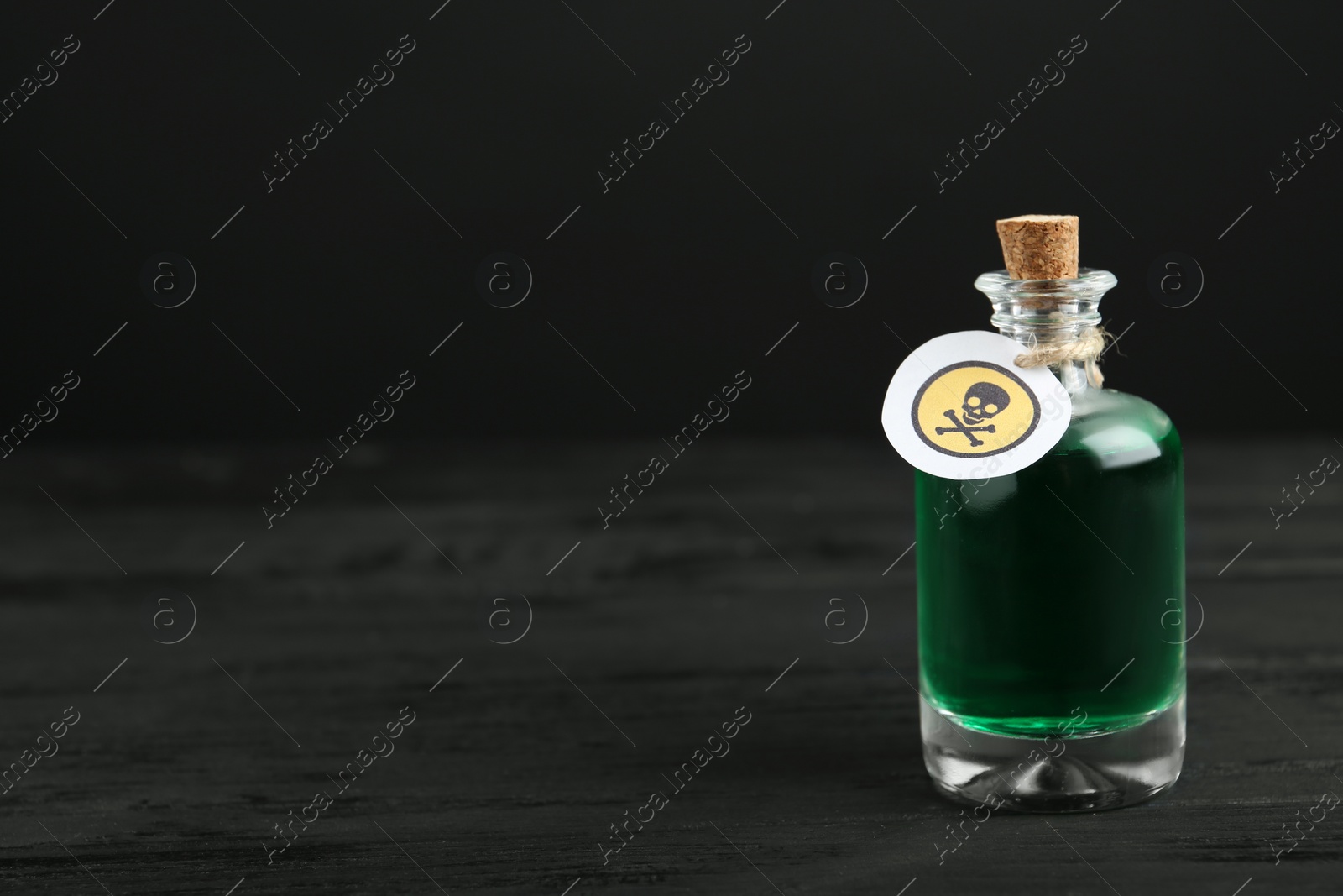 Photo of Glass bottle of poison with warning sign on black wooden table. Space for text