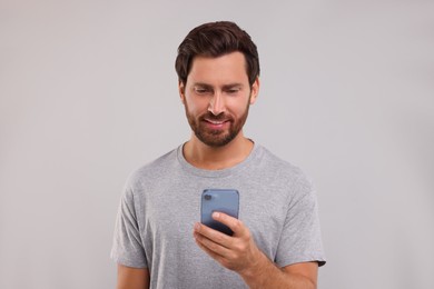 Photo of Handsome bearded man using smartphone on grey background