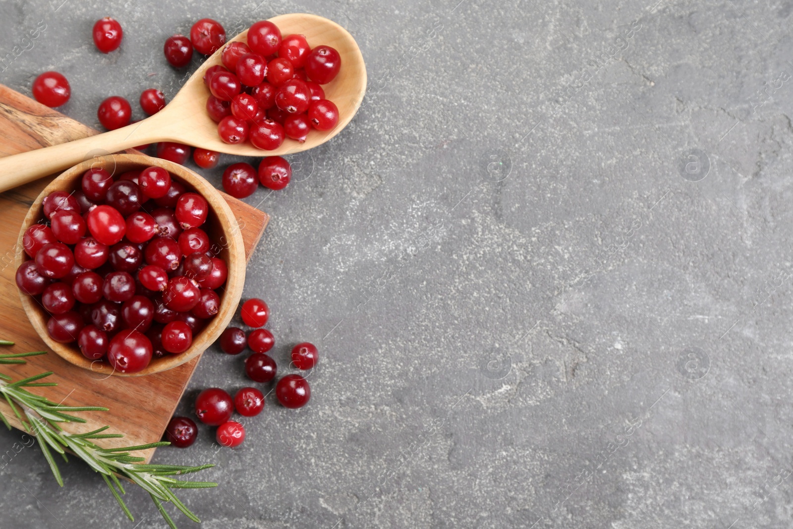 Photo of Fresh ripe cranberries and rosemary on grey table, flat lay. Space for text