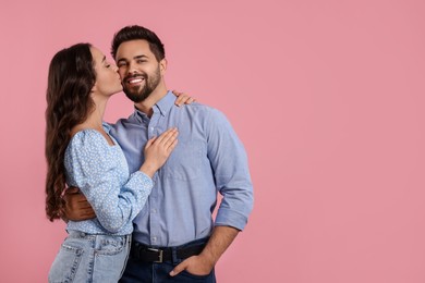 Photo of Woman kissing her smiling boyfriend on pink background. Space for text