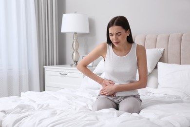 Photo of Young woman suffering from stomach ache in bedroom