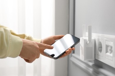 Photo of Woman using smartphone for wireless Wi-Fi repeater indoors, closeup