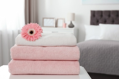 Photo of Stack of clean towels with flower on table in bedroom. Space for text