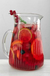 Photo of Glass jug of Red Sangria on white wooden table, closeup