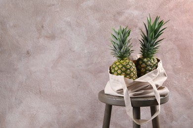 Photo of Bag with delicious ripe pineapples on stand against pink wall. Space for text