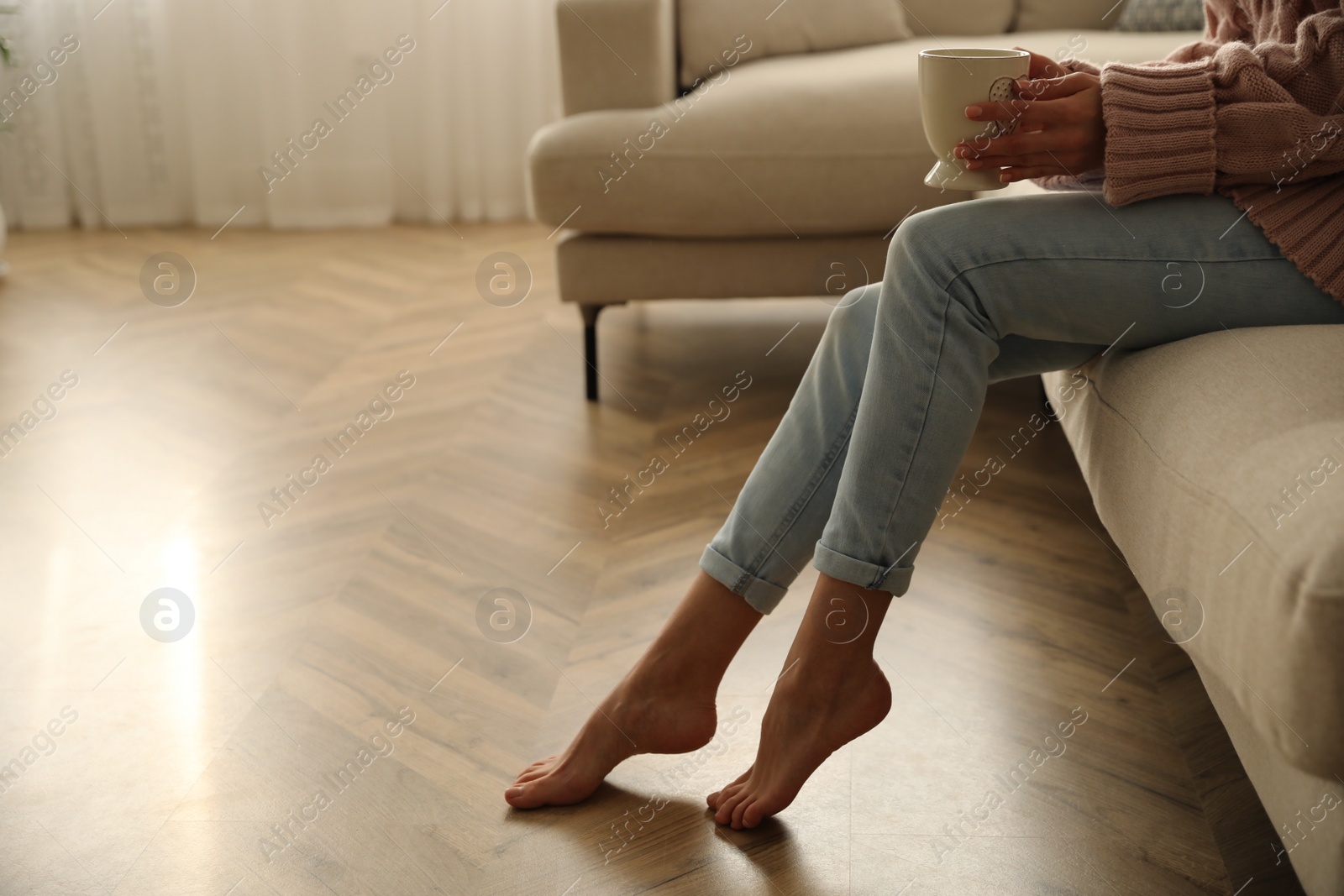 Photo of Barefoot woman sitting on sofa in living room, closeup. Floor heating system