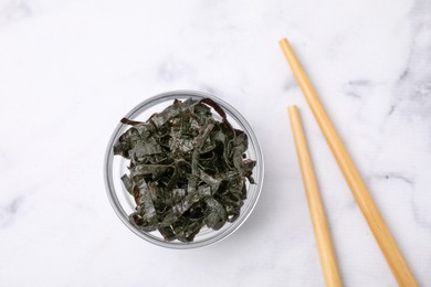 Photo of Chopped nori sheets with chopsticks on white marble table, flat lay
