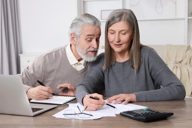 Photo of Elderly couple with papers and laptop discussing pension plan at wooden table in room