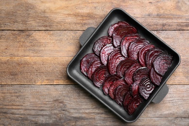 Photo of Baking dish with roasted beetroot slices on wooden table, top view. Space for text