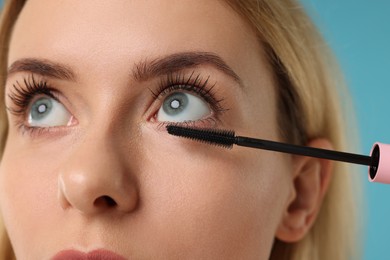 Beautiful woman applying mascara on light blue background, closeup