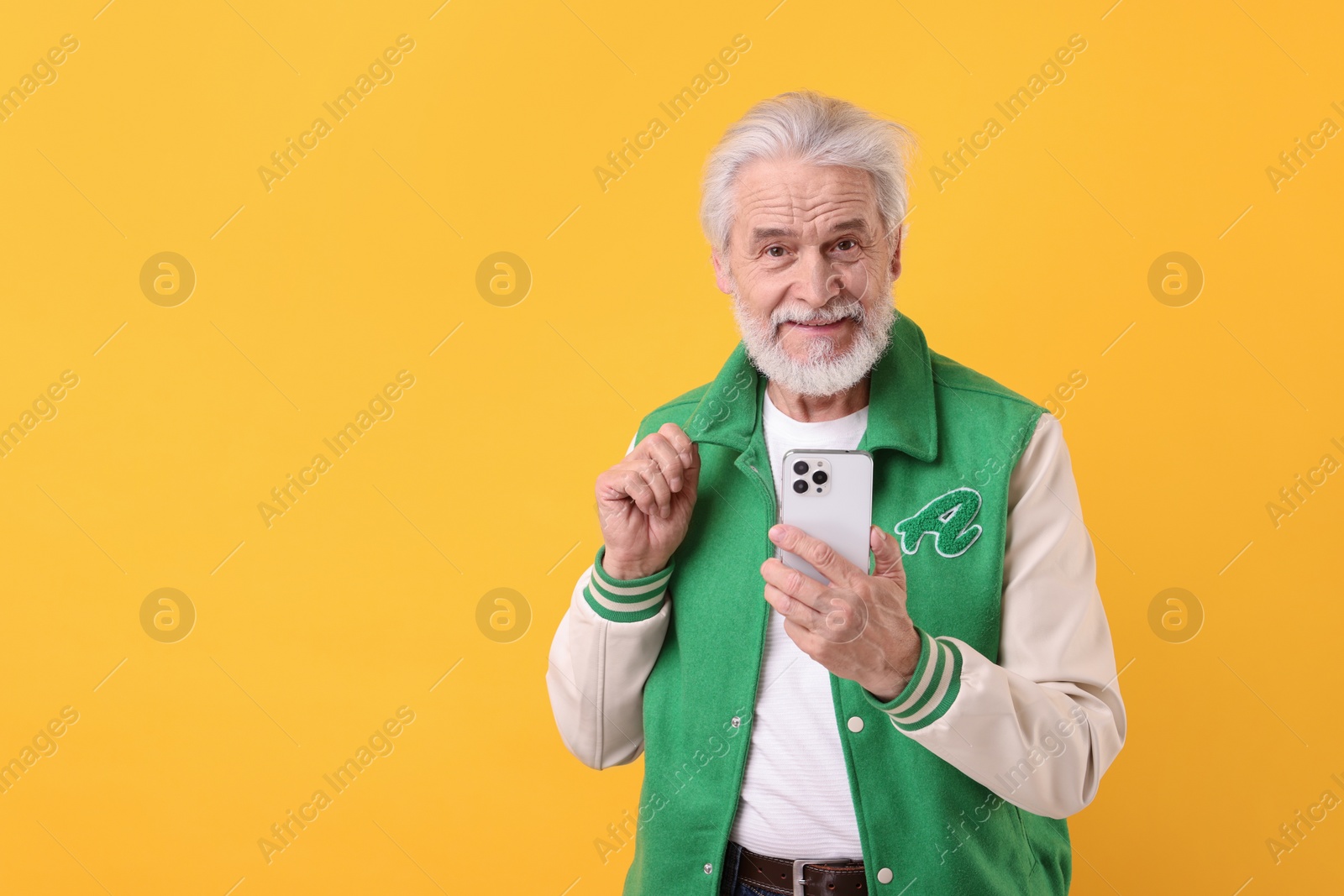 Photo of Portrait of stylish grandpa using smartphone on yellow background, space for text