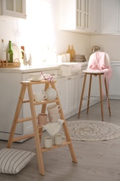 Decorative ladder with different dishware and field flowers bouquet in stylish kitchen. Idea for interior design