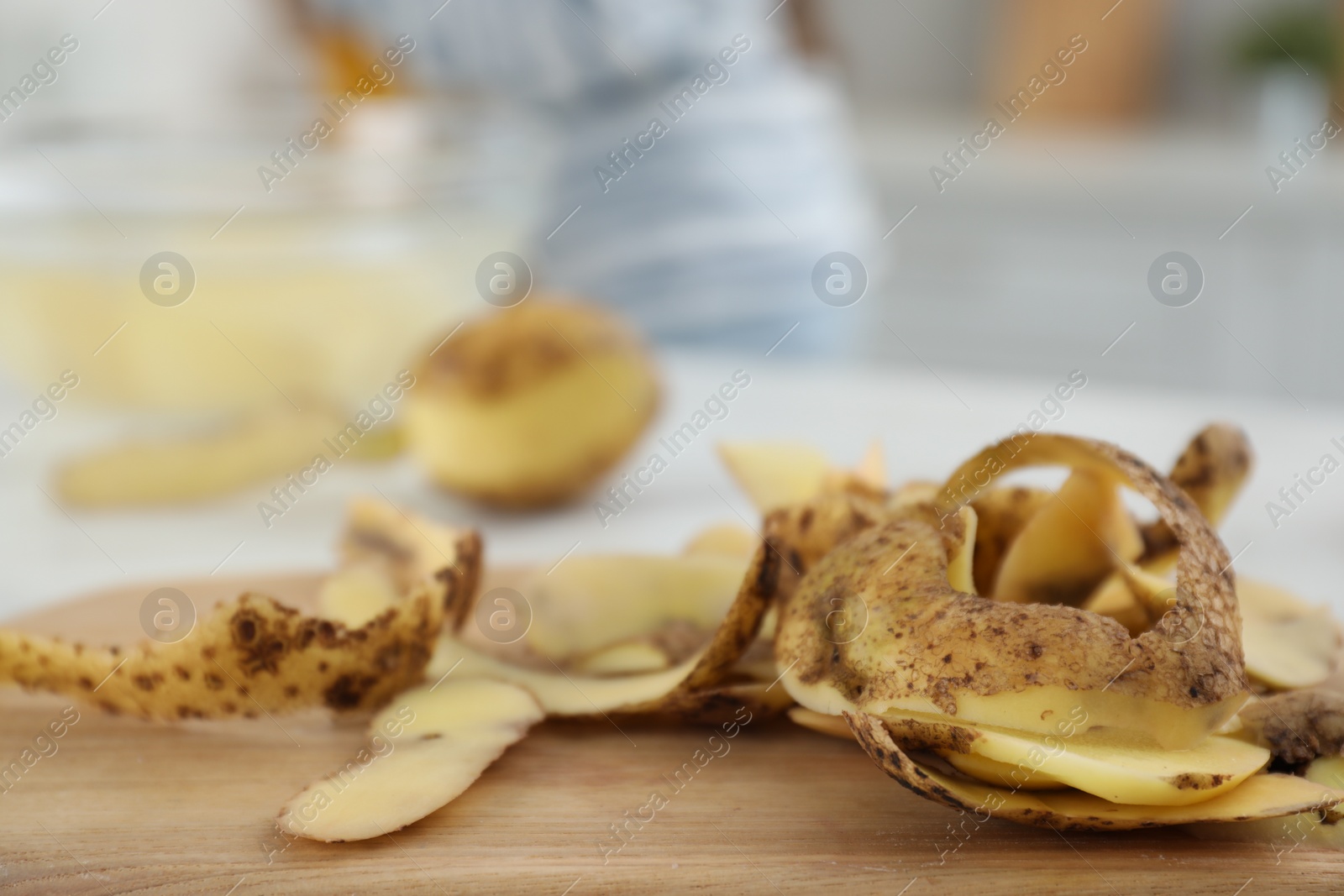 Photo of Wooden board with potato peels on table in kitchen, closeup