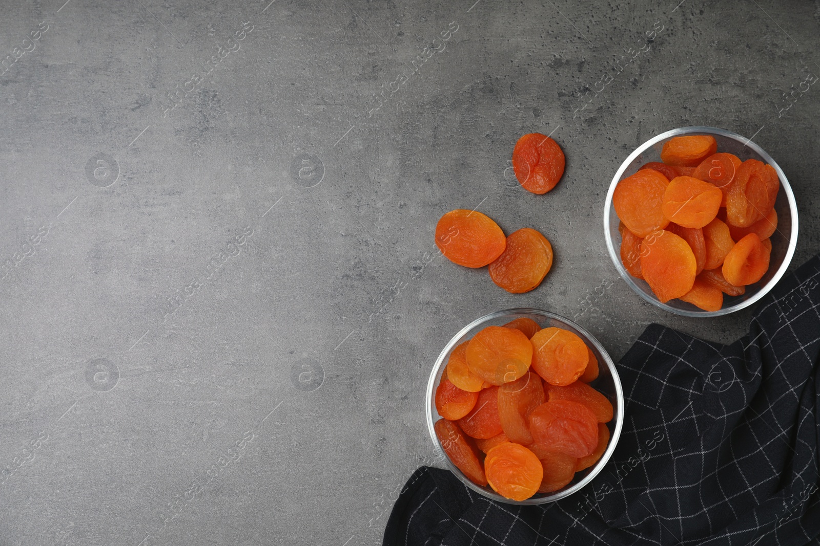 Photo of Bowls of dried apricots on grey table, top view with space for text. Healthy fruit