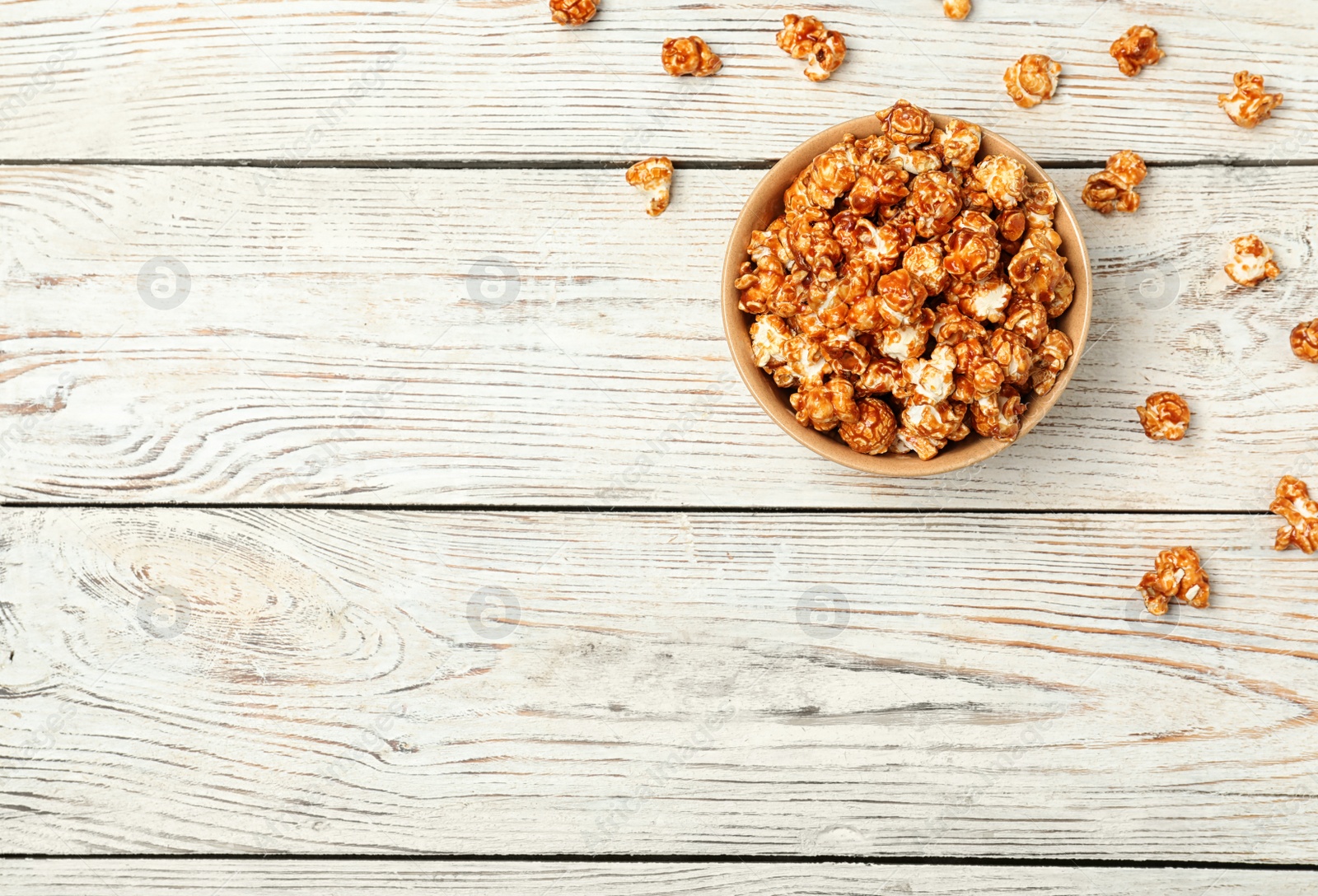 Photo of Bowl with caramel popcorn on white wooden background, top view. Space for text