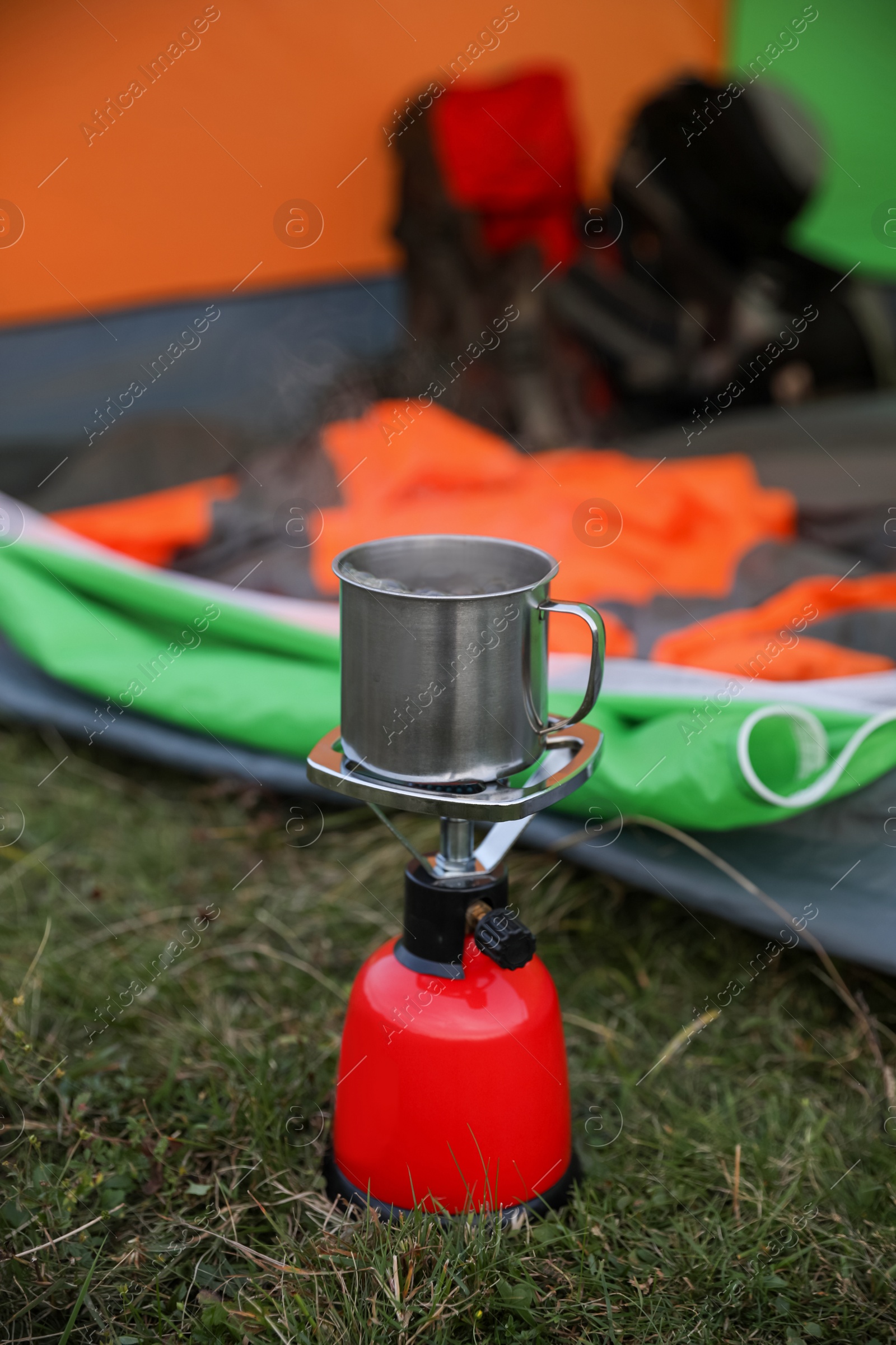 Photo of Boiling drink in metal mug on camping stove near tent outdoors