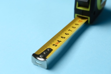 Photo of Tape measure on light blue background, closeup. Construction tool