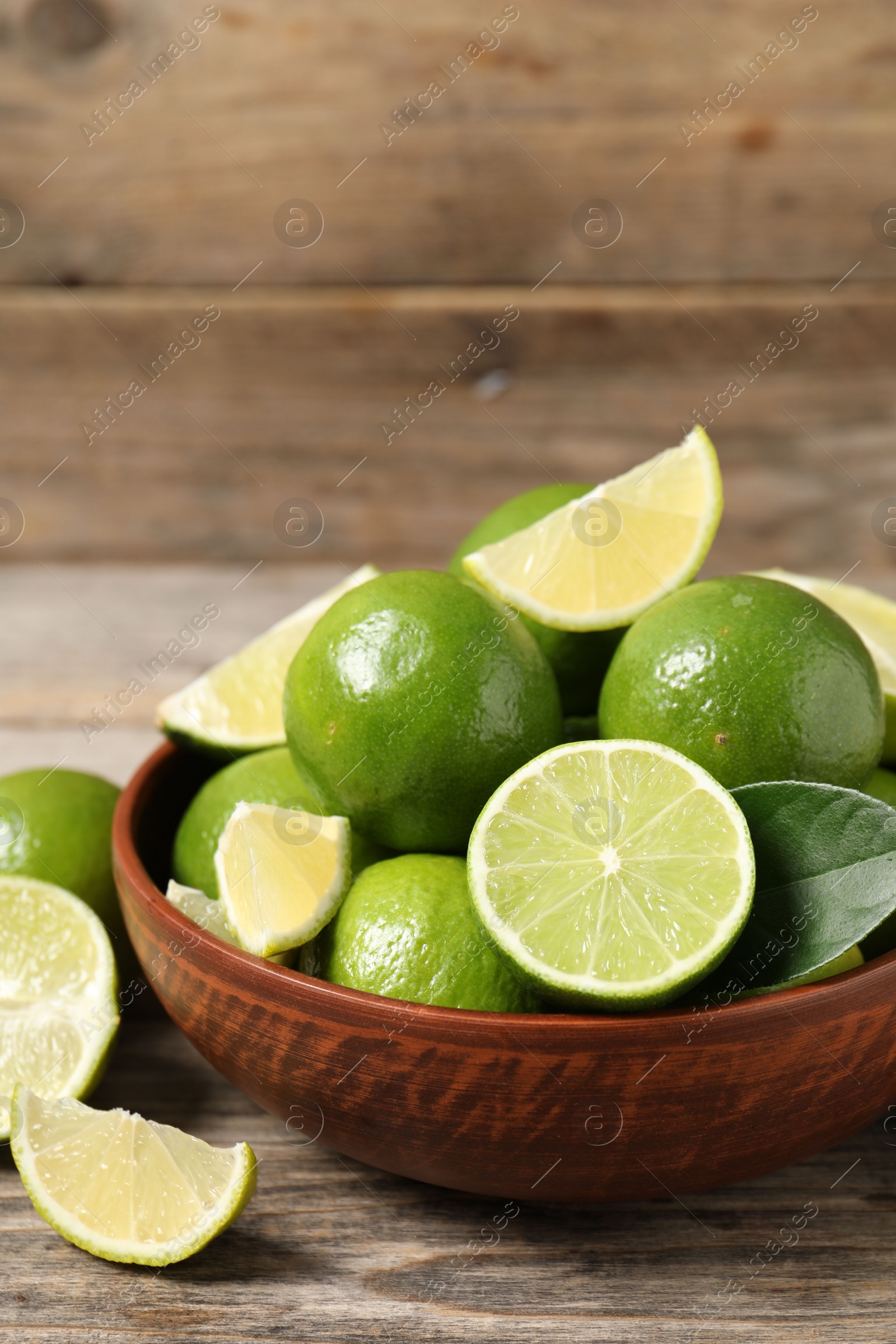 Photo of Tasty ripe limes in bowl on wooden table, closeup