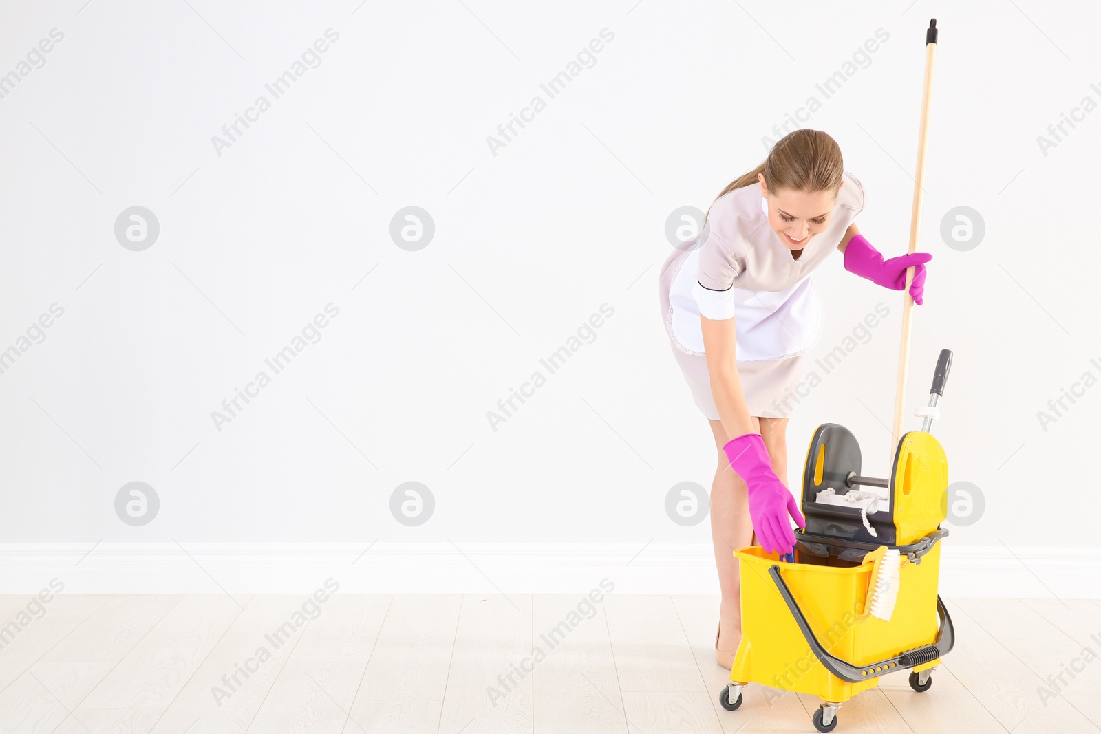 Photo of Young chambermaid with cleaning supplies indoors