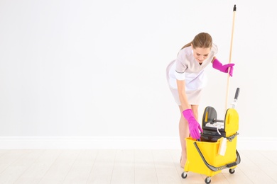 Young chambermaid with cleaning supplies indoors