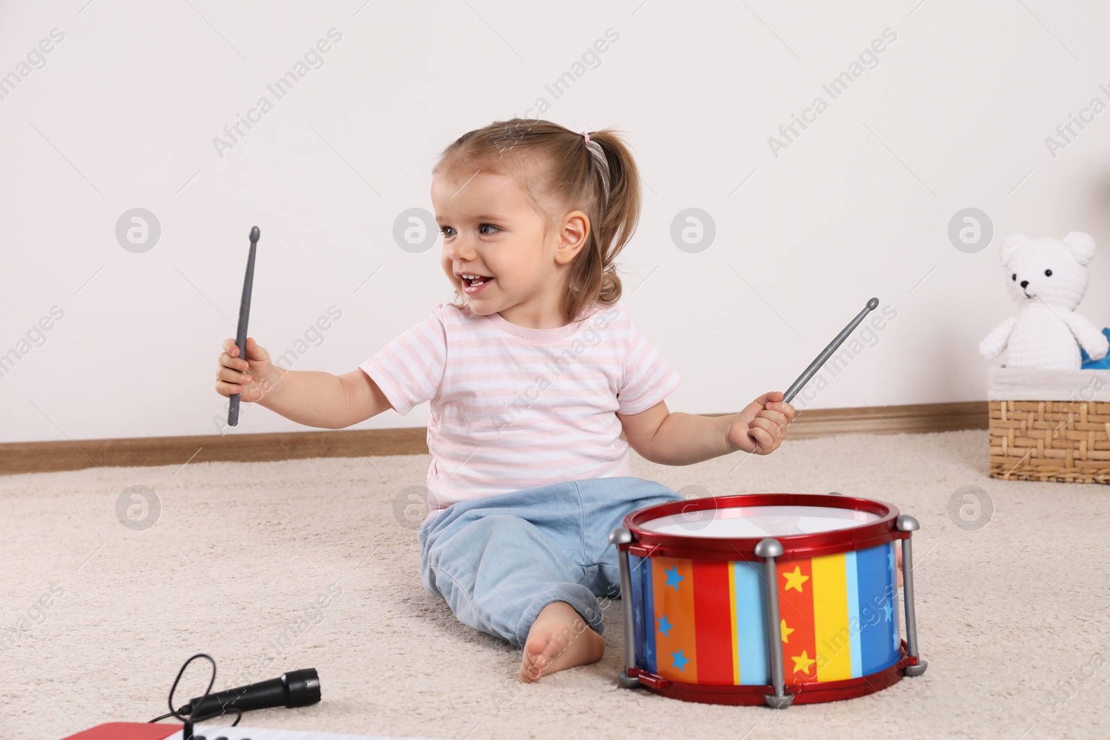 Photo of Cute little girl playing with drum and drumsticks at home