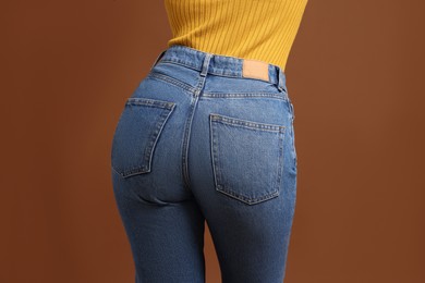 Photo of Woman in stylish jeans on brown background, closeup