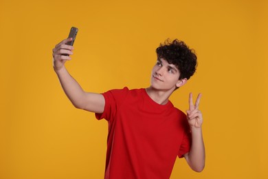 Photo of Teenage boy taking selfie and showing peace gesture on orange background