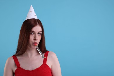 Photo of Sad woman in party hat with blower on light blue background, space for text
