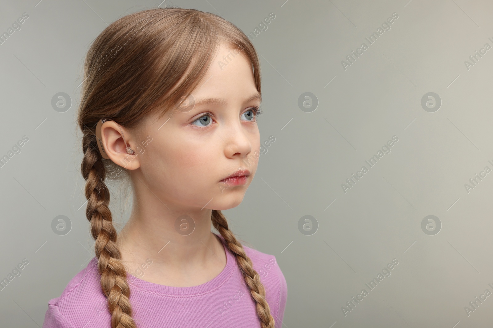 Photo of Little girl with hearing aid on grey background. Space for text