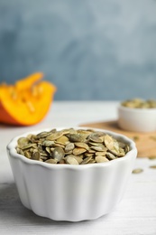 Photo of Bowl of raw pumpkin seeds on white wooden table against blue background. Space for text