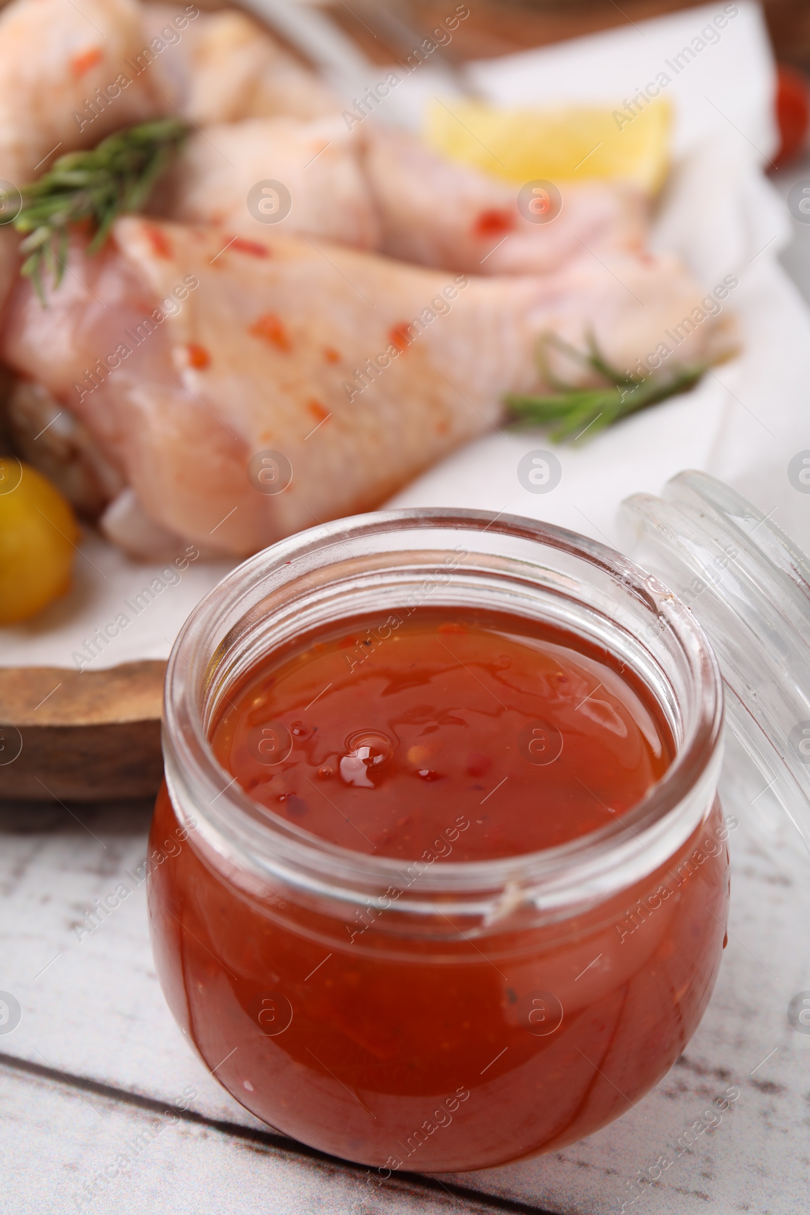 Photo of Marinade and raw chicken drumsticks on white wooden table, closeup