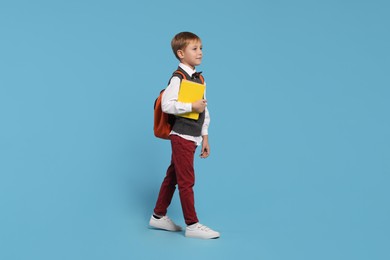 Happy schoolboy with backpack and books on light blue background
