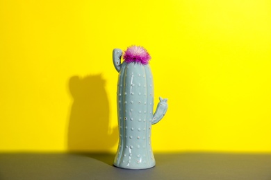 Trendy cactus shaped ceramic vase with flower on table against color background