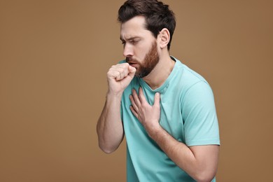 Photo of Sick man coughing on brown background. Cold symptoms