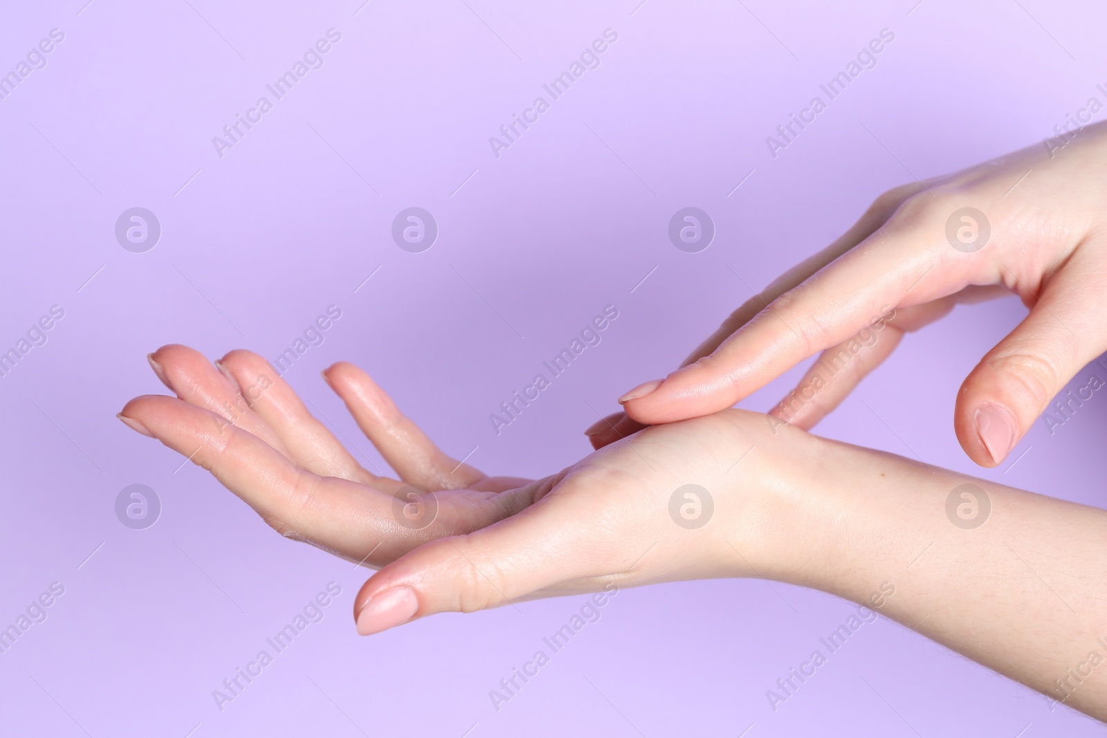 Photo of Woman applying cream on her hand against violet background, closeup