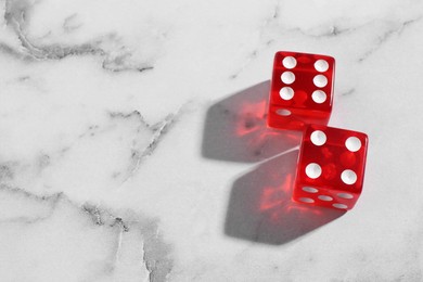 Photo of Two red game dices on white marble table, above view. Space for text