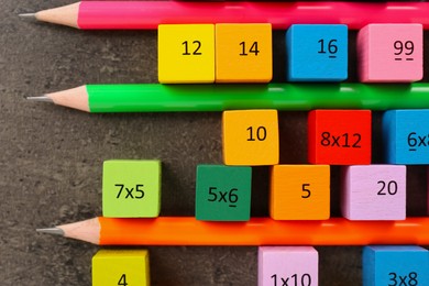 Photo of Many colorful cubes with numbers, multiplications and pencils on dark grey table, flat lay
