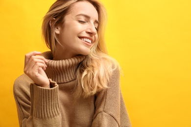 Photo of Beautiful young woman wearing knitted sweater on yellow background. Space for text