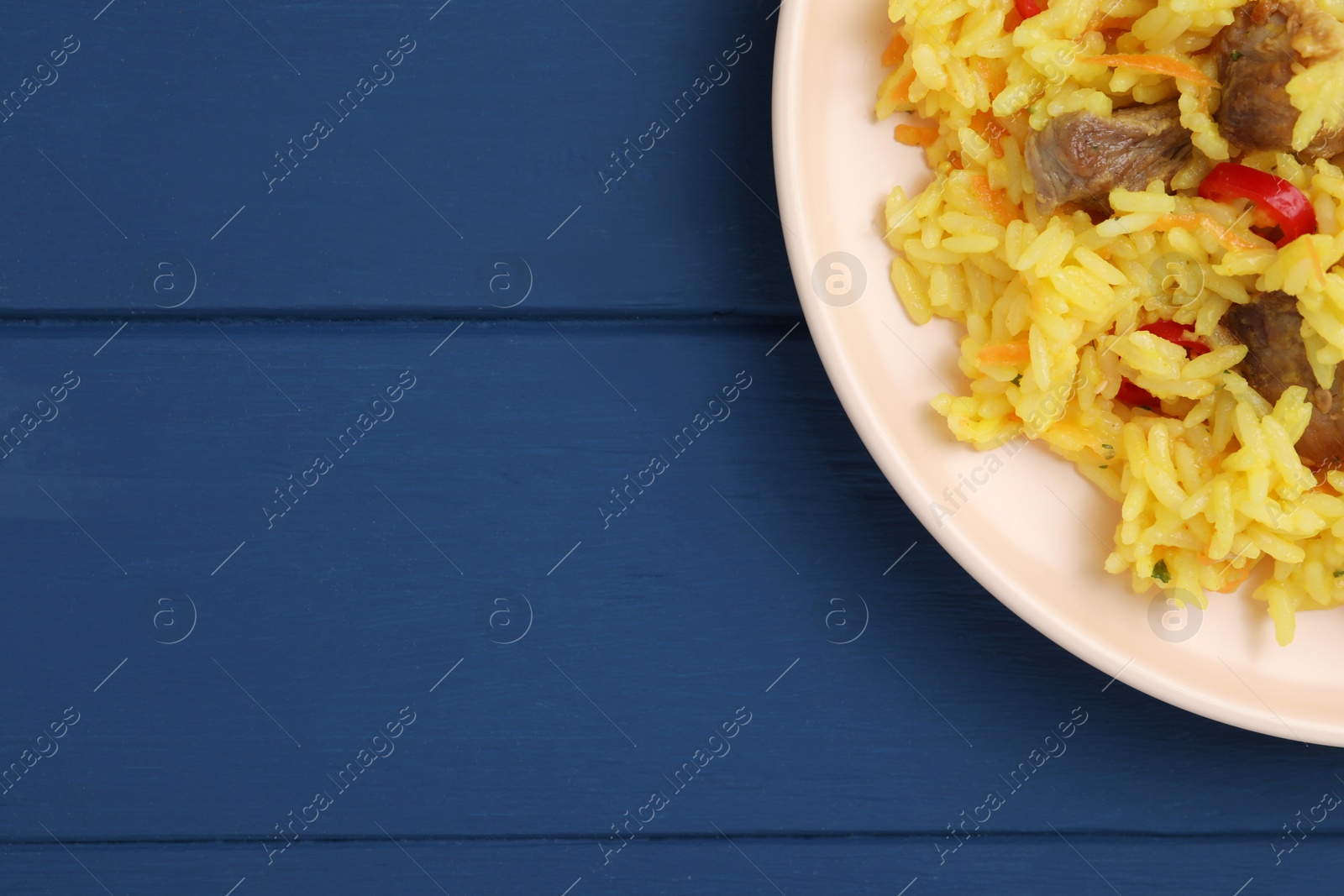 Photo of Delicious pilaf with meat on blue wooden table, top view. Space for text