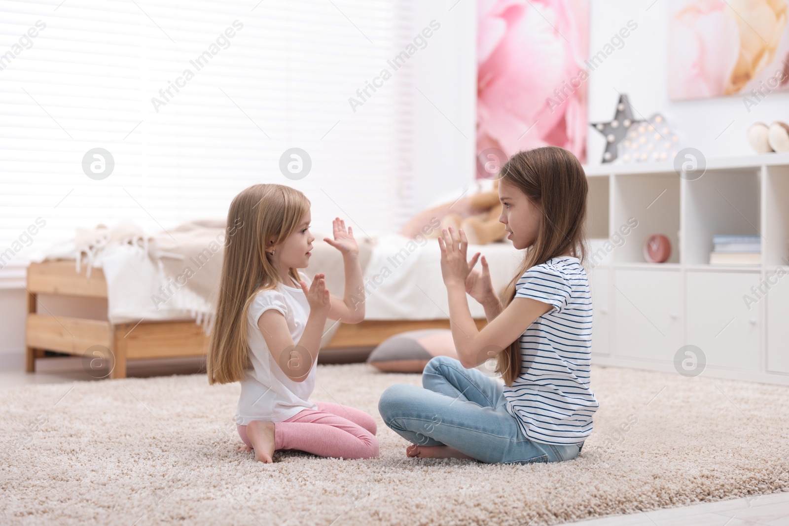 Photo of Cute little sisters playing clapping game with hands at home