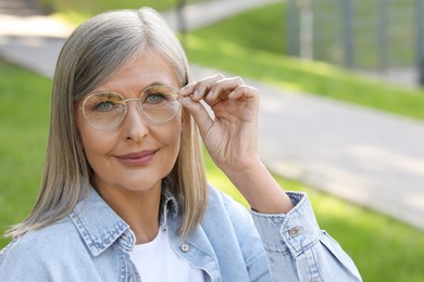 Portrait of beautiful senior woman in glasses outdoors, space for text