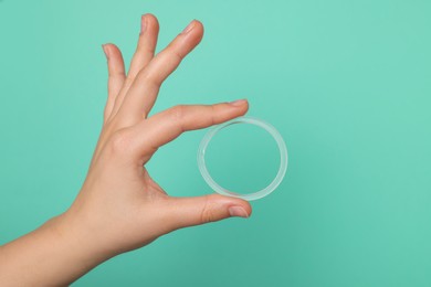 Woman holding diaphragm vaginal contraceptive ring on turquoise background, closeup. Space for text