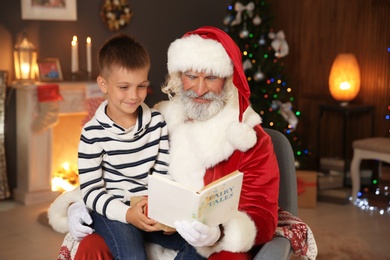 Photo of Little child with Santa Claus reading Christmas story at home