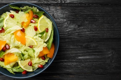 Photo of Delicious salad with Chinese cabbage, lemon, persimmon and pomegranate seeds on black wooden table, top view. Space for text